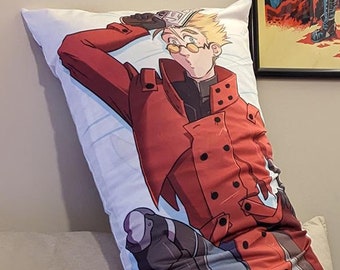 May include: A white body pillow with a printed image of an anime character wearing a red coat and black pants. The character has blonde hair and is sitting with their legs crossed.