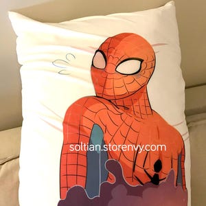 Puede incluir: Una funda de almohada blanca con una ilustración de Spiderman roja y azul. La ilustración muestra la cabeza y el torso de Spiderman, con los brazos extendidos. El texto "soltian.storenvy.com" está impreso en la funda de almohada.