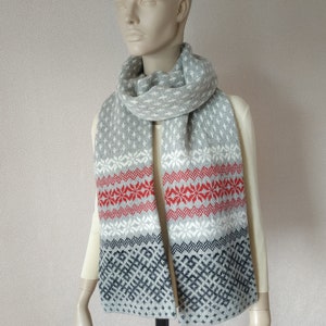 Könnte beinhalten: Ein grauer Strick Schal mit einem weißen und roten geometrischen Muster. Der Schal ist gefaltet und um den Hals einer Schaufensterpuppe gelegt.