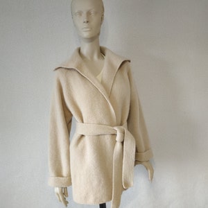 Op de afbeelding: Een beige gebreide cardigan met een shawlkraag en een strikceintuur. De cardigan is gemaakt van een zacht, comfortabel materiaal en heeft een ontspannen pasvorm.