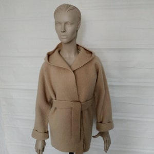 Op de afbeelding: Een beige capuchonjas met een strikceintuur. De jas is gemaakt van een zacht, pluche materiaal.