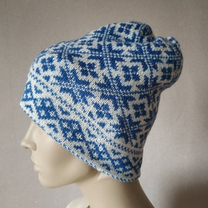 Op de afbeelding: Een witte en blauwe gebreide muts met een sneeuwvlokkenpatroon.