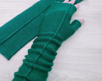 以下が含まれることがあります： リブ編みでできた緑色の指なし手袋のペア。手袋は編み物で、各手袋の中央に縫い目があります。