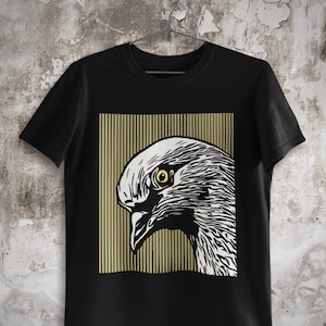 May include: Black t-shirt featuring a graphic print of a white dove's head with a yellow eye, set against a background of gold stripes.