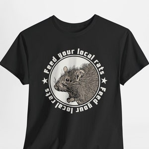Black t-shirt featuring a circular design with an illustrated rat in the center, encircled by the phrase Feed your local rats. The design has a vintage punk aesthetic with cream coloured accents, standing out sharply against the black background