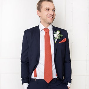 The front-view model with a suit wears the same aurora red color linen necktie, pocket square, and linen aurora red color suspenders with clips.