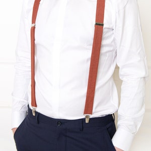 May include: A white dress shirt with a pair of brown suspenders. The suspenders have silver clips and are attached to the shirt and pants.