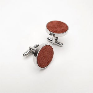 May include: A pair of silver cufflinks with round, orange fabric insets.
