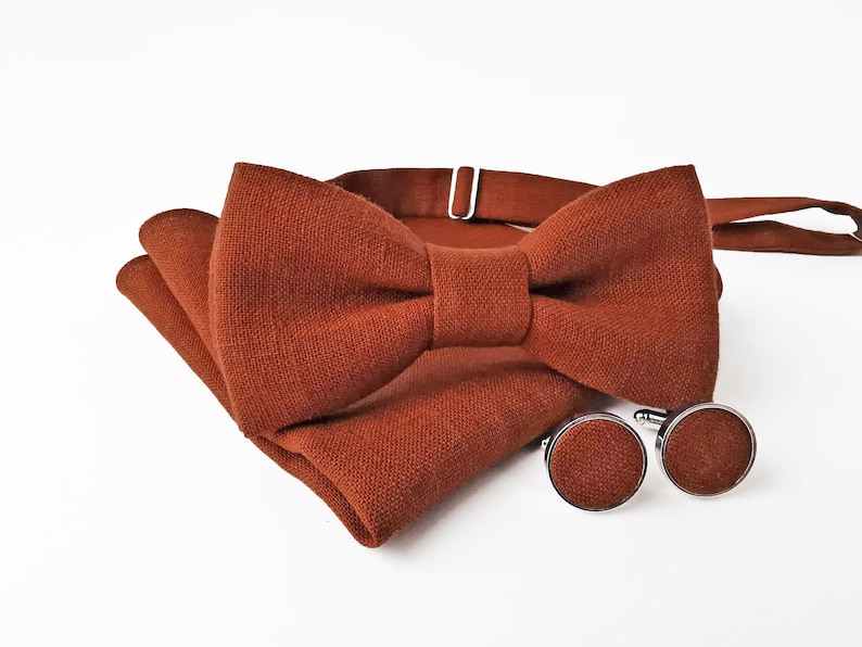 May include: A brown linen bow tie with matching pocket square and cufflinks. The bow tie has a simple design and is perfect for a formal occasion.