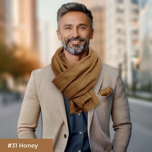 May include: A man wearing a brown scarf over a beige blazer and a dark blue shirt. #31 Honey