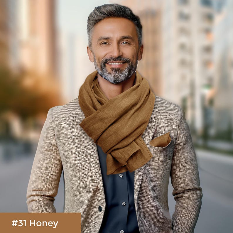 May include: A man wearing a brown scarf over a beige blazer and a dark blue shirt. #31 Honey