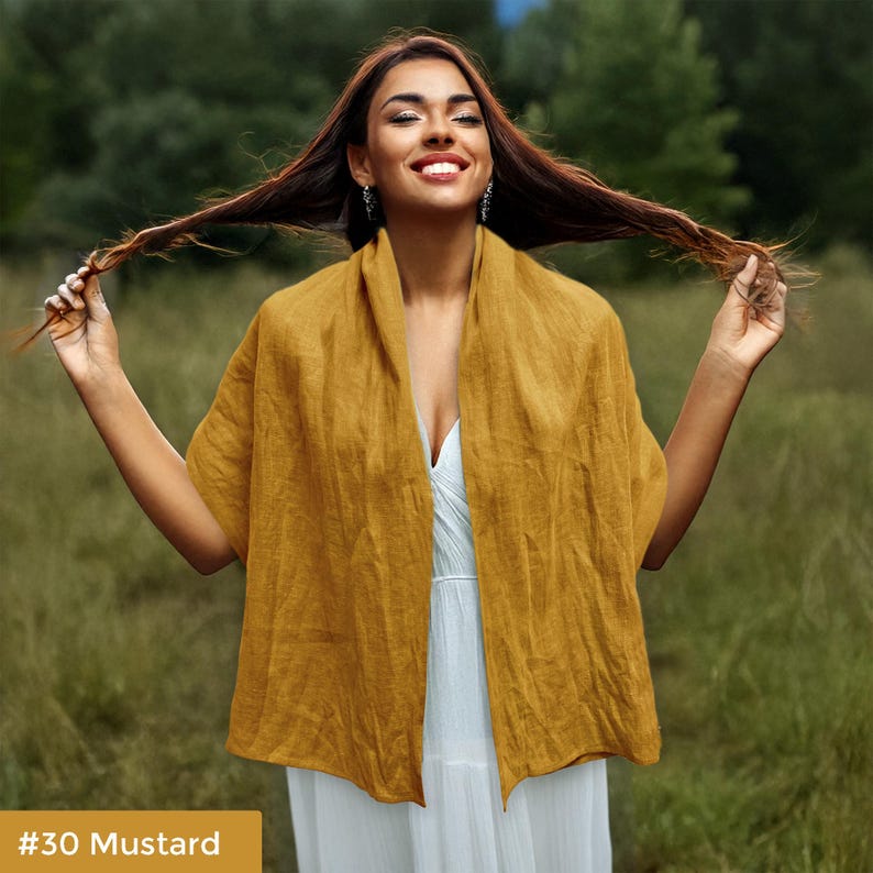 May include: A mustard yellow linen scarf draped around a person's shoulders. The scarf is made of a soft, lightweight fabric and has a simple, elegant design.