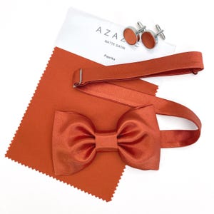 Może przedstawiać: Muszka w kolorze wypalanej pomarańczy z dopasowanym materiałem i spinkami do mankietów. Próbka materiału ma nadrukowany tekst "AZAZE MATTE SATIN Paprika".