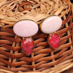 May include: A pair of earrings featuring a pink oval-shaped stone and a teardrop-shaped red stone.