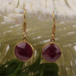 May include: A pair of gold earrings with a red gemstone dangle. The earrings have a simple design and are perfect for everyday wear.
