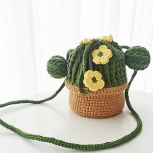 Puede incluir: Una bolsa de crochet verde en forma de cactus con detalles de flores amarillas y una maceta de crochet marrón. La bolsa tiene una correa larga verde.