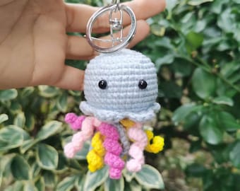 May include: A crocheted jellyfish keychain with a light blue body, black eyes, and pink, yellow, and white tentacles.