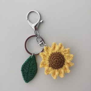 May include: A crocheted sunflower keyring with a green leaf charm and a silver key ring.