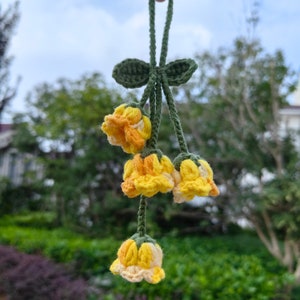 May include: A crocheted flower bouquet charm with yellow and orange flowers and green leaves. The charm is hanging from a green string.