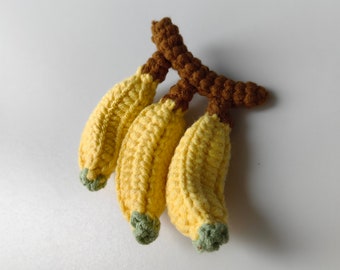 May include: A bunch of three crocheted yellow bananas with brown stems. The bananas are made with a soft yarn and have a realistic appearance.