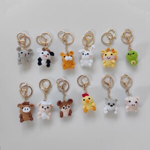 May include: A collection of crochet animal keychains, including a mouse, cow, tiger, rabbit, giraffe, frog, bull, sheep, bear, chicken, wolf, and pig. Each keychain has a gold-colored ring.
