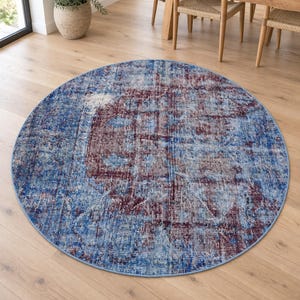 Könnte beinhalten: Ein runder Teppich mit einem abgenutzten, vintage-inspirierten Muster in den Farben Dunkelburgunder, Marineblau und verblasstem Hellblau. Der Teppich hat eine kurzflorige Textur mit einem sich wiederholenden geometrischen und floralen Motiv.