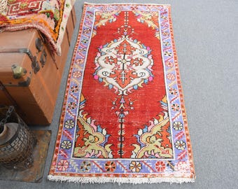 Puede incluir: Una alfombra rectangular roja desgastada con un diseño central de medallón blanco y naranja. La alfombra presenta un borde con patrones florales y geométricos en azul, amarillo y rosa. La alfombra mide aproximadamente 120 cm de largo.