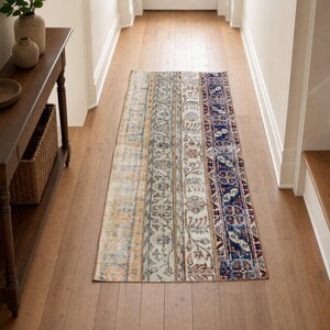 May include: A rectangular runner rug featuring a vertical patchwork design with multiple distinct sections. The pattern includes faded orange, cream, and light blue floral motifs alongside a bold, dark blue band with intricate red and white details.