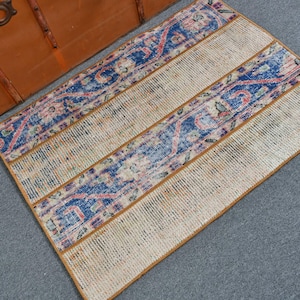 May include: A rectangular rug with a beige background and three vertical stripes. The central stripe and the two outer stripes feature a blue and pink floral pattern. The rug is bordered with a brown trim.