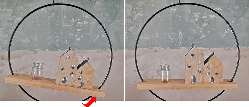 May include: A circular black metal frame holds a horizontal wooden shelf. On the shelf sit two wooden house-shaped blocks with painted windows and doors, alongside a small, clear glass jar. The shelf is suspended within the metal ring.