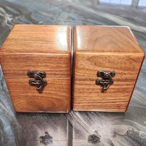 May include: Two wooden boxes with a warm brown finish. Each box has a hinged lid and a decorative metal clasp. The boxes are side-by-side, showcasing the natural wood grain and craftsmanship.