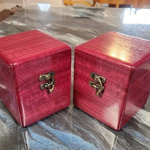 May include: Two small, square, wooden boxes with hinged lids and brass clasps. The boxes are made of a dark purple wood with a rich grain pattern.