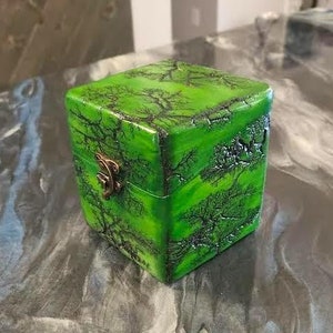 May include: A small, square box with a green and black marbled design. The box has a brass latch and is perfect for storing small items.