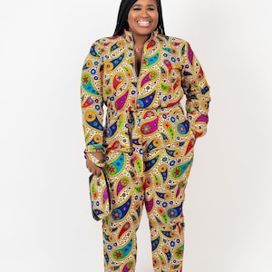 Puede incluir: Una mujer lleva un mono de manga larga con un estampado de paisley en tonos de azul, verde, amarillo, rosa y rojo. El mono tiene una cremallera y un cinturón.