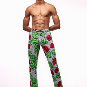 Puede incluir: Pantalones ajustados con un llamativo estampado de hojas verdes y rojas sobre un fondo a rayas grises y blancas. Los pantalones se combinan con zapatos de cuero negro. El estilo general es audaz y llamativo.