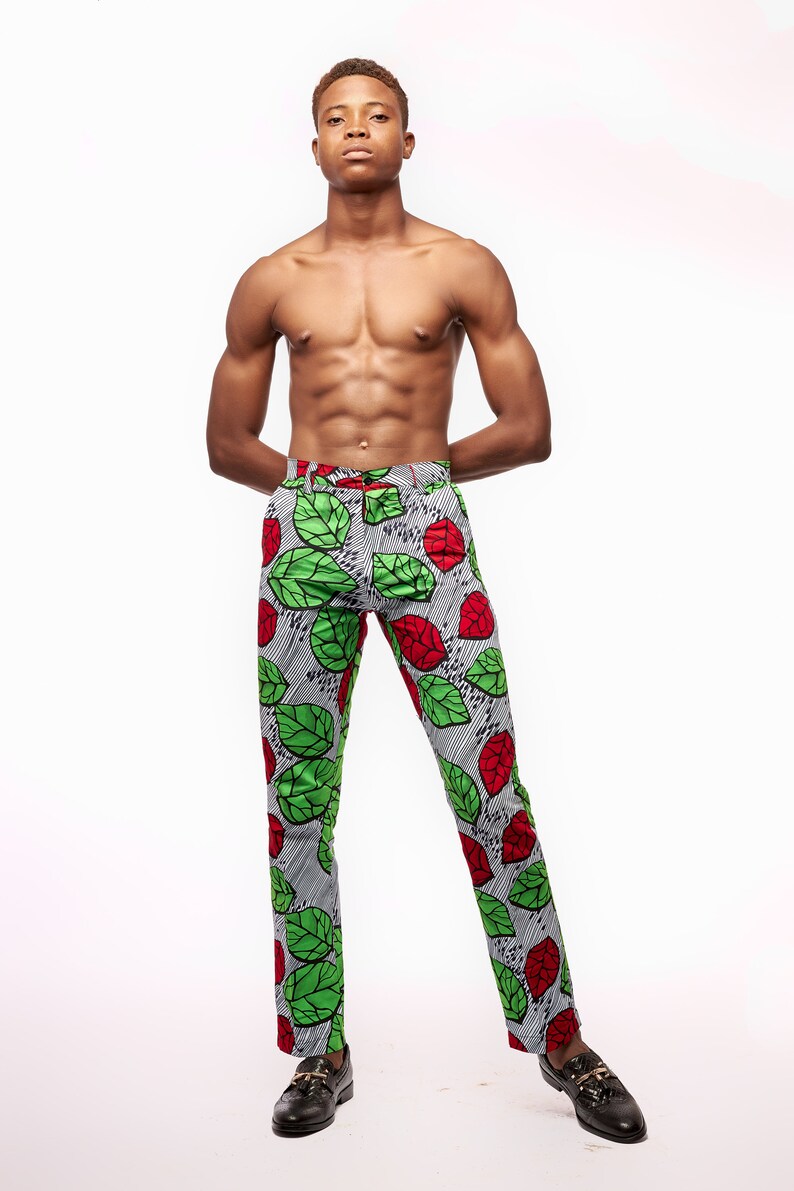 Puede incluir: Pantalones ajustados con un llamativo estampado de hojas verdes y rojas sobre un fondo a rayas grises y blancas. Los pantalones se combinan con zapatos de cuero negro. El estilo general es audaz y llamativo.