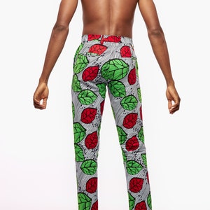 Puede incluir: Pantalones estampados con un patr&oacute;n de hojas rojas y verdes sobre un fondo a rayas blancas y negras. Los pantalones son a medida y parecen estar hechos de una tela ligera. Los pantalones se llevan con zapatos de vestir negros.