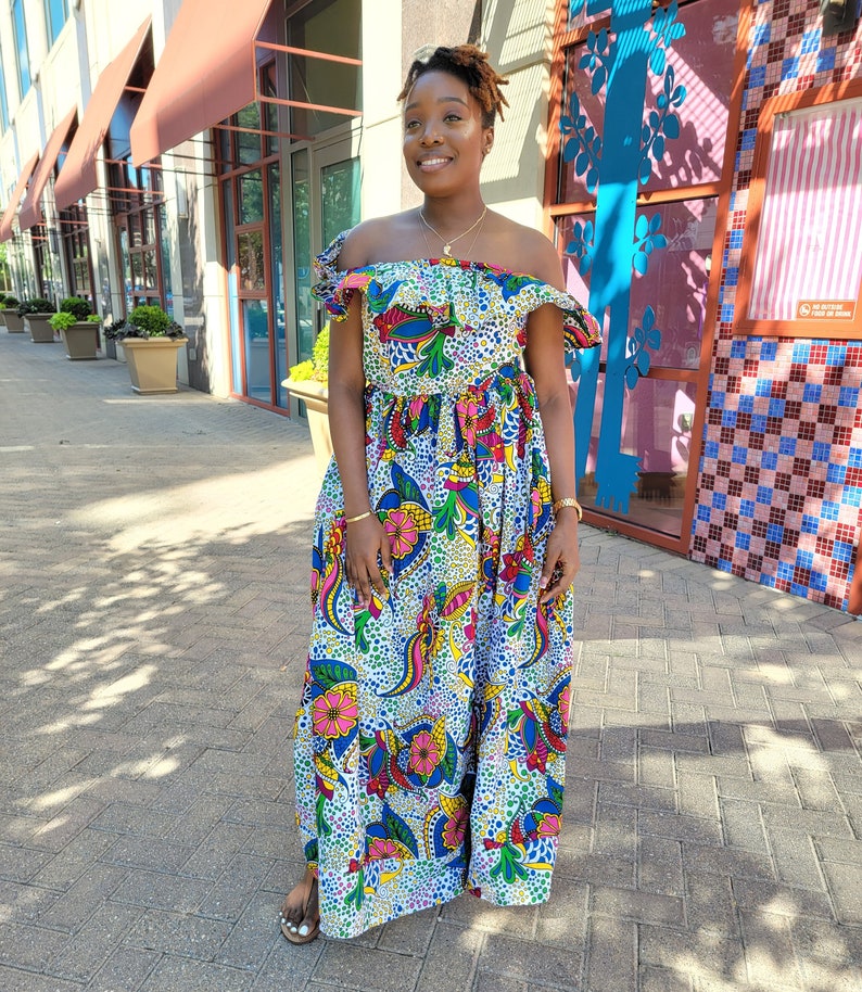 Puede incluir: Un vestido maxi blanco con estampado floral colorido. El vestido tiene un escote de hombros descubiertos con volantes y un corpi&ntilde;o ajustado. La falda es amplia y fluida.