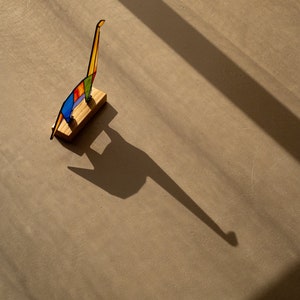 May include: A colorful glass sculpture of a giraffe standing on a wooden base. The sculpture is casting a long shadow on the floor.