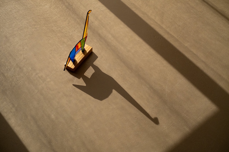 May include: A colorful glass sculpture of a giraffe standing on a wooden base. The sculpture is casting a long shadow on the floor.