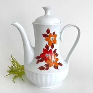 May include: White ceramic coffee pot with a floral design featuring orange and red flowers with brown leaves. The pot has a lid and a handle.