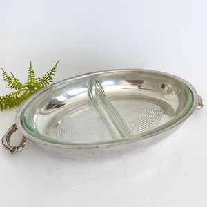 Op de afbeelding: Ovale verzilverde serveerschaal met een helder glazen inzetstuk verdeeld in twee secties. Het glazen inzetstuk heeft een spiraalvormig ontwerp. De schaal heeft handvatten aan elke kant en staat tegen een witte achtergrond.