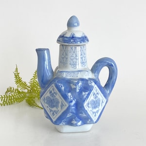 Puede incluir: Una tetera pequeña de cerámica azul y blanca con tapa. La tetera tiene un diseño geométrico con motivos florales.