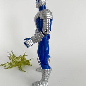 K&ouml;nnte beinhalten: Eine blaue und silberne Actionfigur von Spider-Man, die eine silberne R&uuml;stung tr&auml;gt. Die Figur ist mit erhobenem rechten Arm und dem linken Arm, der im Ellbogen gebeugt ist, aufgestellt.