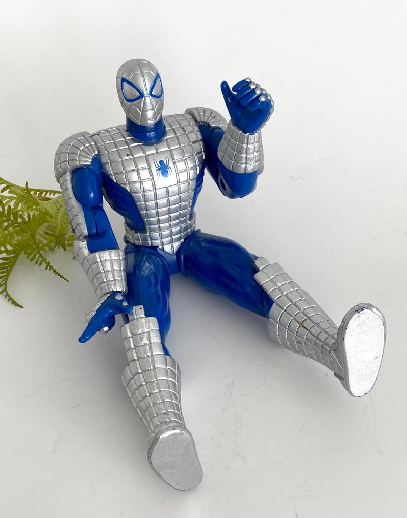 K&ouml;nnte beinhalten: Eine blaue und silberne Actionfigur von Spider-Man, die eine silberne R&uuml;stung tr&auml;gt. Die Figur sitzt mit dem rechten Arm erhoben in einer Daumen-hoch-Geste.