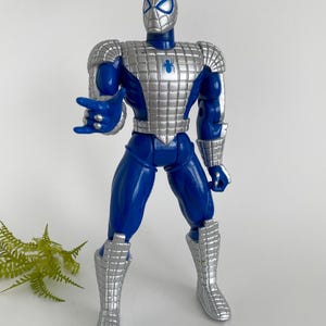 K&ouml;nnte beinhalten: Blaue und silberne Actionfigur von Spider-Man, der einen silbernen Anzug tr&auml;gt. Die Figur hat ein Spinnenlogo auf der Brust und ist mit ausgestreckten Armen posiert.