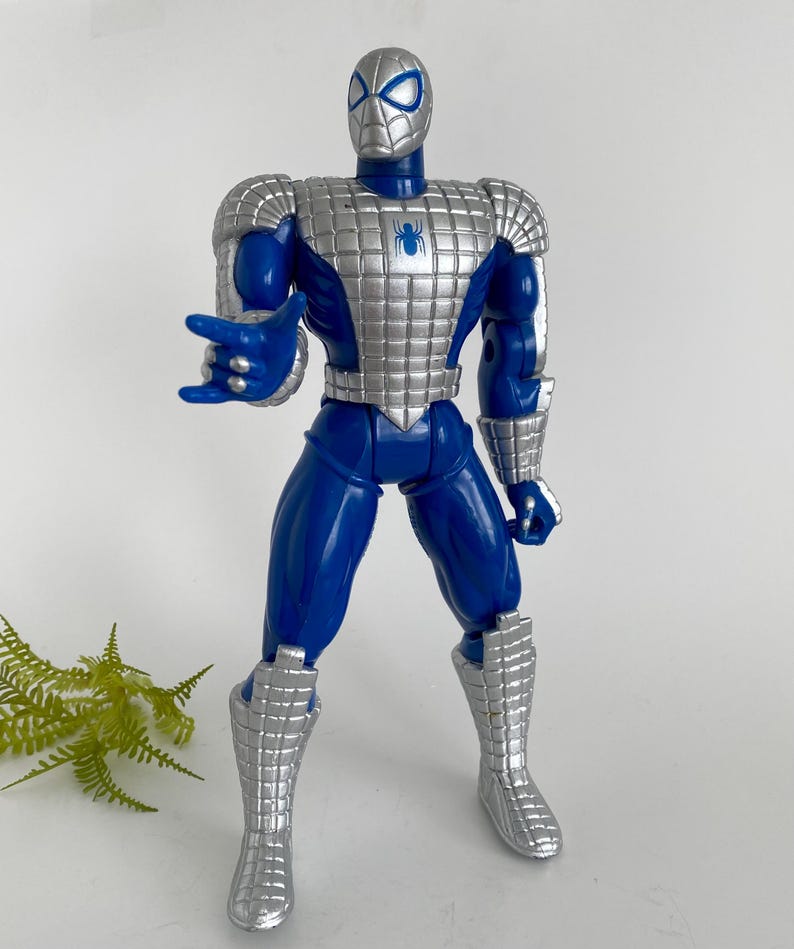 K&ouml;nnte beinhalten: Blaue und silberne Actionfigur von Spider-Man, der einen silbernen Anzug tr&auml;gt. Die Figur hat ein Spinnenlogo auf der Brust und ist mit ausgestreckten Armen posiert.