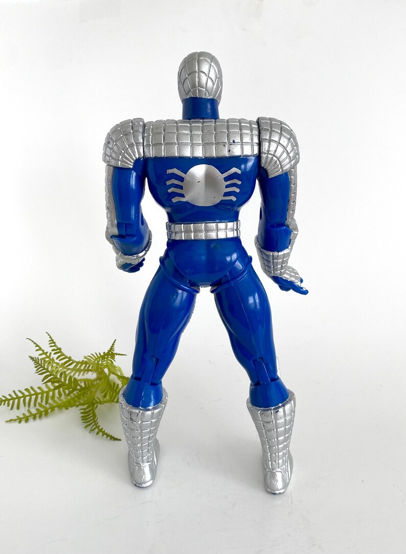 K&ouml;nnte beinhalten: Eine blaue und silberne Actionfigur von Spider-Man, die eine silberne R&uuml;stung tr&auml;gt. Die Figur ist mit den Armen an den Seiten und leicht gespreizten Beinen aufgestellt.