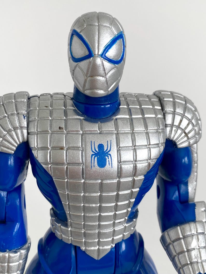 K&ouml;nnte beinhalten: Eine blaue und silberne Actionfigur von Spider-Man, die eine silberne R&uuml;stung mit einem Spinnenlogo auf der Brust tr&auml;gt.