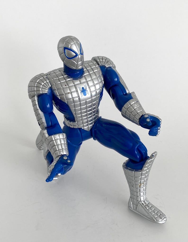 K&ouml;nnte beinhalten: Eine blaue und silberne Actionfigur von Spider-Man in einer knienden Pose. Die Figur tr&auml;gt einen silbernen Anzug mit einem blauen Spinnenlogo auf der Brust.